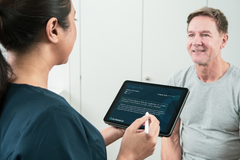 A clinician advising a patient. She is holding a tablet with text on it and facing the patient who is smiling.