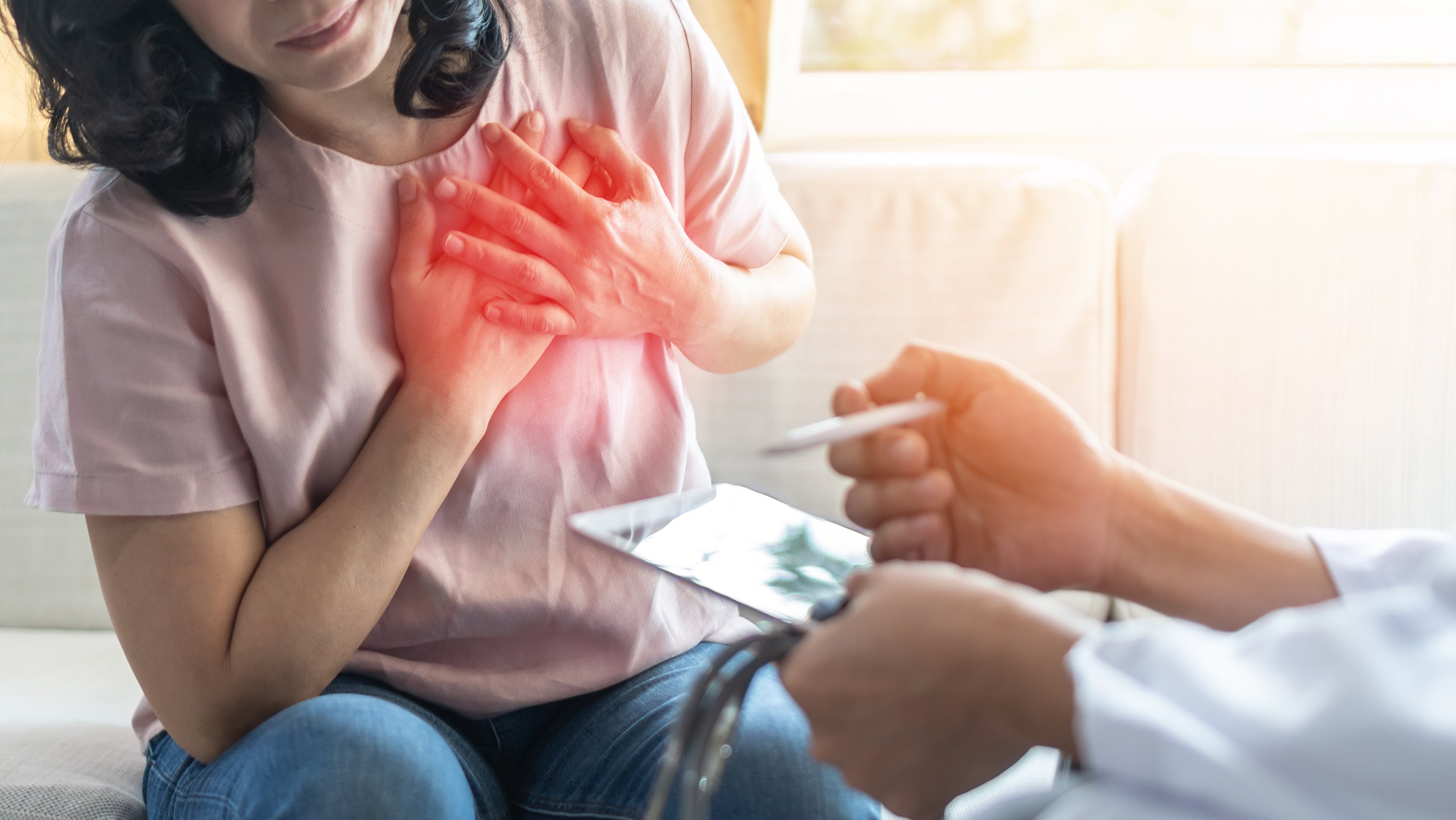 A woman holding her hands against her chest and a cardiologist looking on with a tablet in hand.